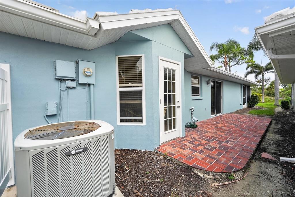 A light blue house exterior features a brick patio, a Trane AC unit, and windows — 746 HARRINGTON LAKE DRIVE N UNIT 117, VENICE, FL