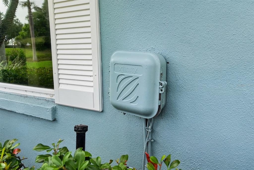 An Xfinity utility box is mounted on the exterior blue stucco wall of a house — 746 HARRINGTON LAKE DRIVE N UNIT 117, VENICE, FL