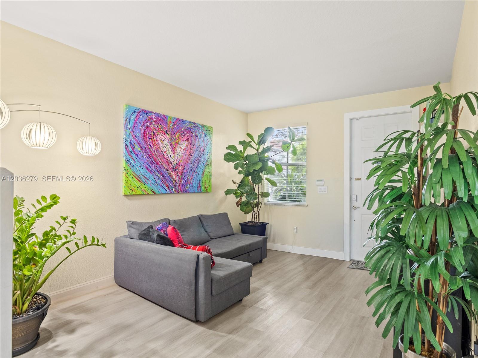 A living room features a gray sectional sofa, a large heart painting, and two potted plants — 8128 NW 108th Ct # 8128, Doral FL 33178, DORAL, FL