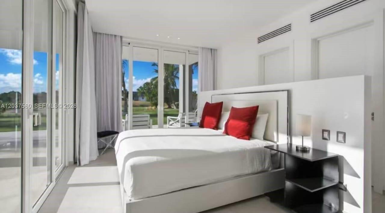 A modern bedroom features a white bed with red pillows, floor-to-ceiling windows, and white walls — 0 Caleton estate 1, FL