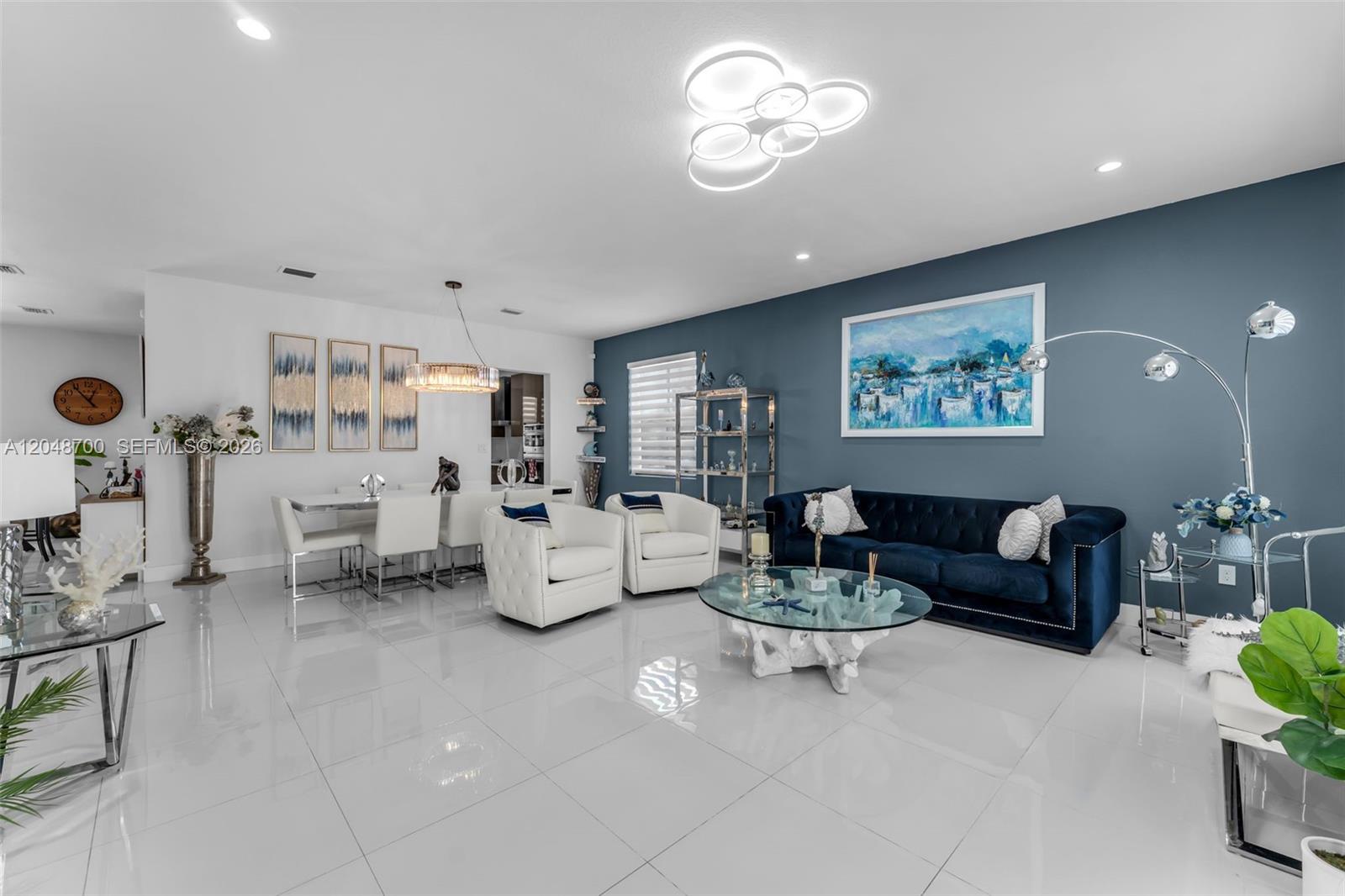 A modern living and dining area features white tile floors, a blue accent wall, and contemporary furniture — 1810 SW 144th Ave, Miami FL 33175, MIAMI, FL