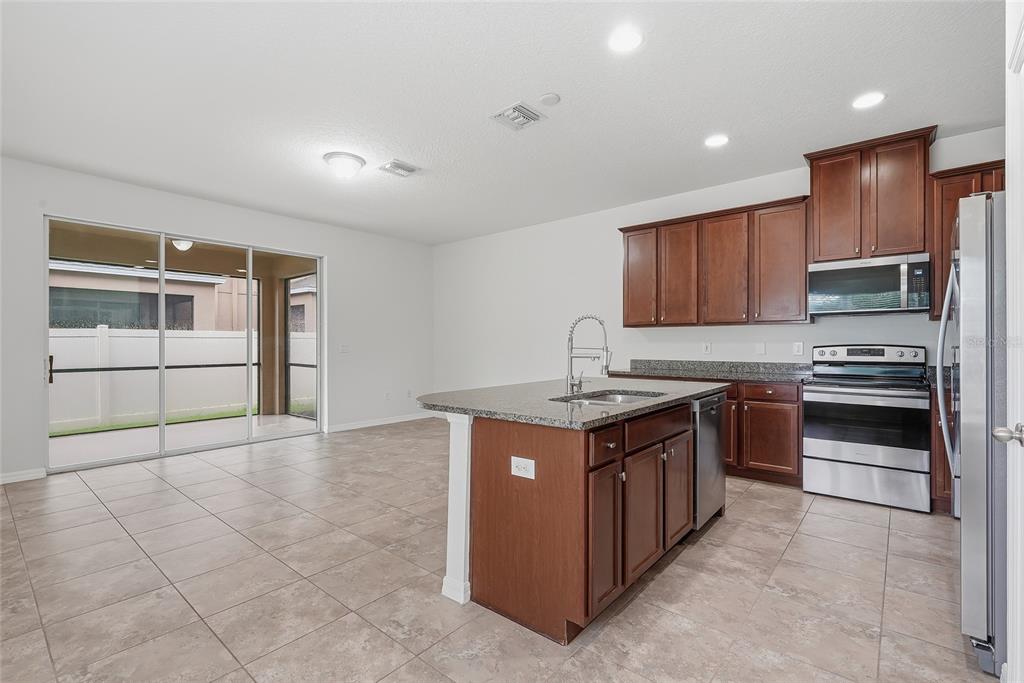 A kitchen with dark wood cabinets, granite countertops, and a center island opens to a patio — 4097 70TH TERRACE N, PINELLAS PARK, FL