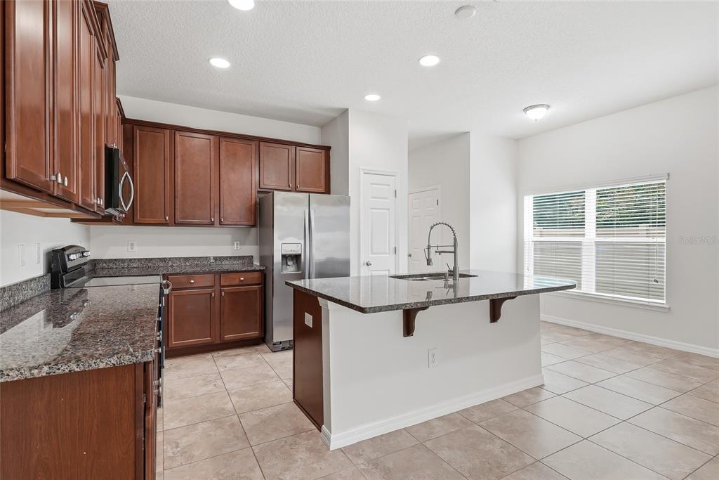 A kitchen with dark wood cabinets, granite countertops, a center island, and tile flooring — 4097 70TH TERRACE N, PINELLAS PARK, FL