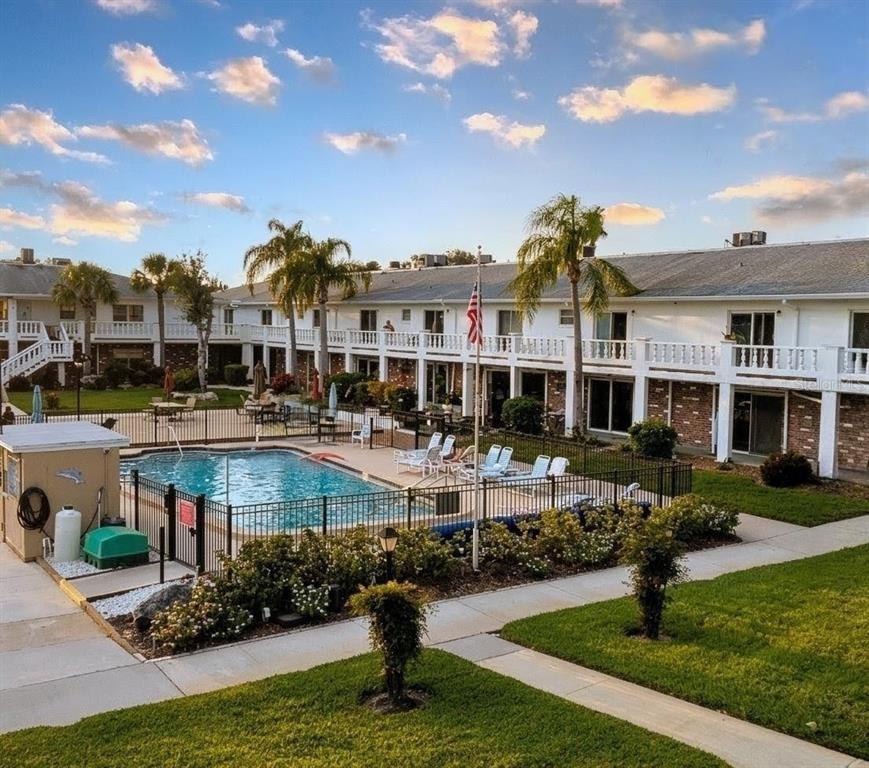 A swimming pool sits in the courtyard of a two-story apartment complex with palm trees — 4744 AZALEA DRIVE UNIT 204, NEW PORT RICHEY, FL