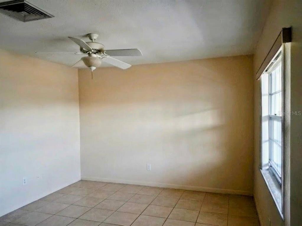 An empty room with beige walls, tile flooring, a ceiling fan, and a window — 4744 AZALEA DRIVE UNIT 204, NEW PORT RICHEY, FL