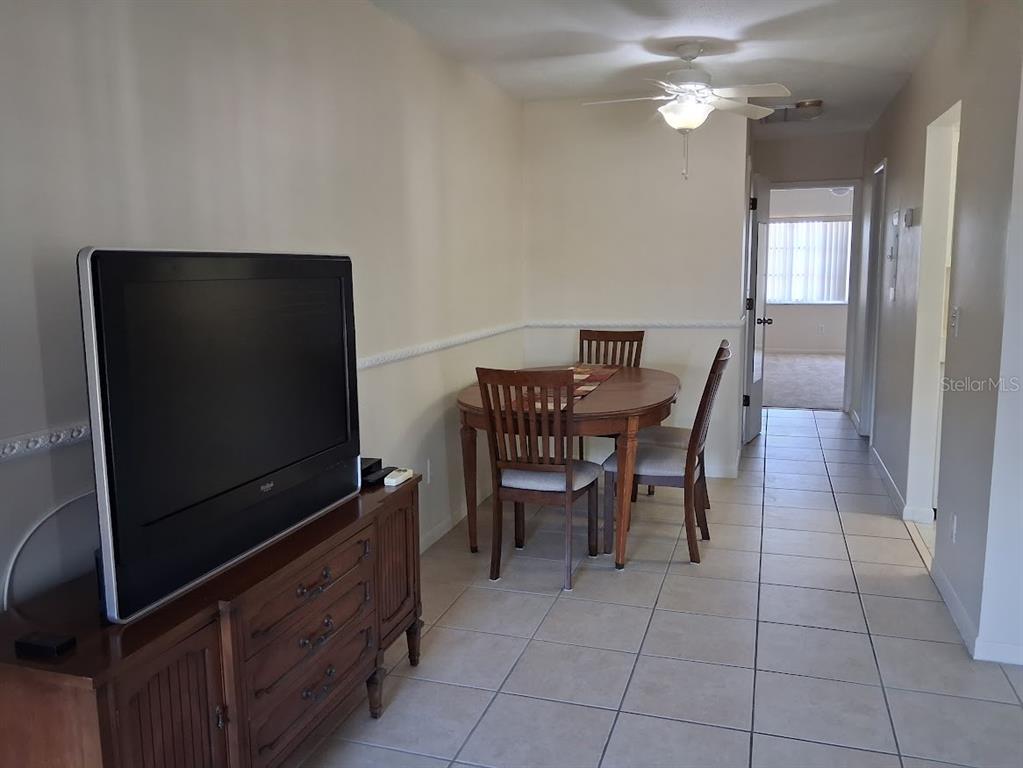 A dining area with a wooden table and chairs sits next to a television console — 4744 AZALEA DRIVE UNIT 204, NEW PORT RICHEY, FL