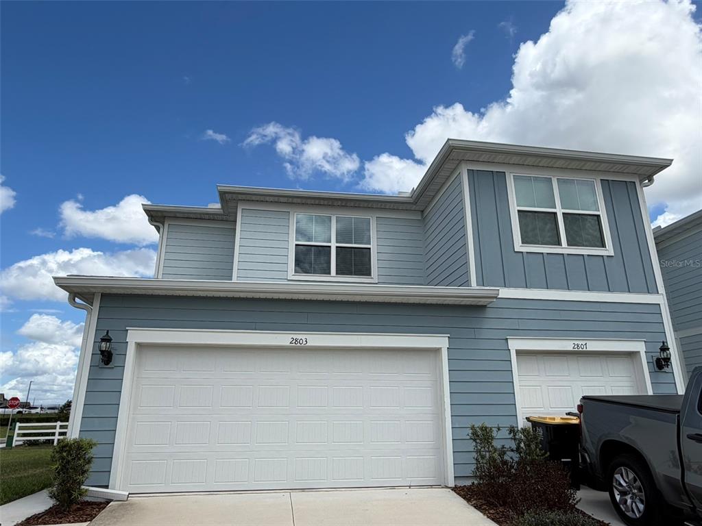 A two-story blue house with two garage doors under a bright, cloudy sky — 2803 STUNNING AVENUE, DAVENPORT, FL