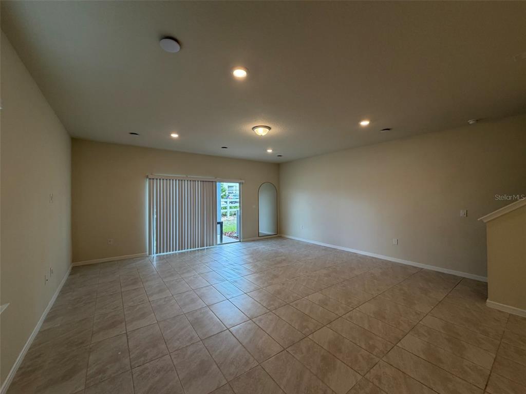 An empty living room features beige tile flooring, recessed lighting, and a sliding glass door — 2803 STUNNING AVENUE, DAVENPORT, FL