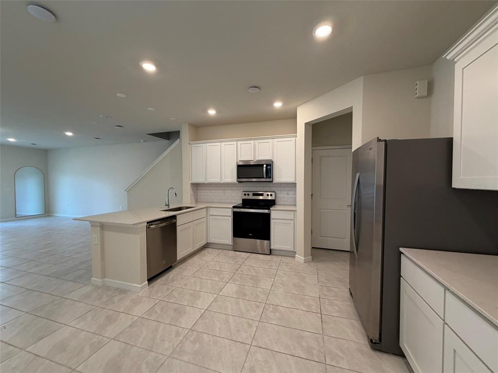 A kitchen with white cabinets, stainless steel appliances, and tile flooring opens to a living area — 2803 STUNNING AVENUE, DAVENPORT, FL