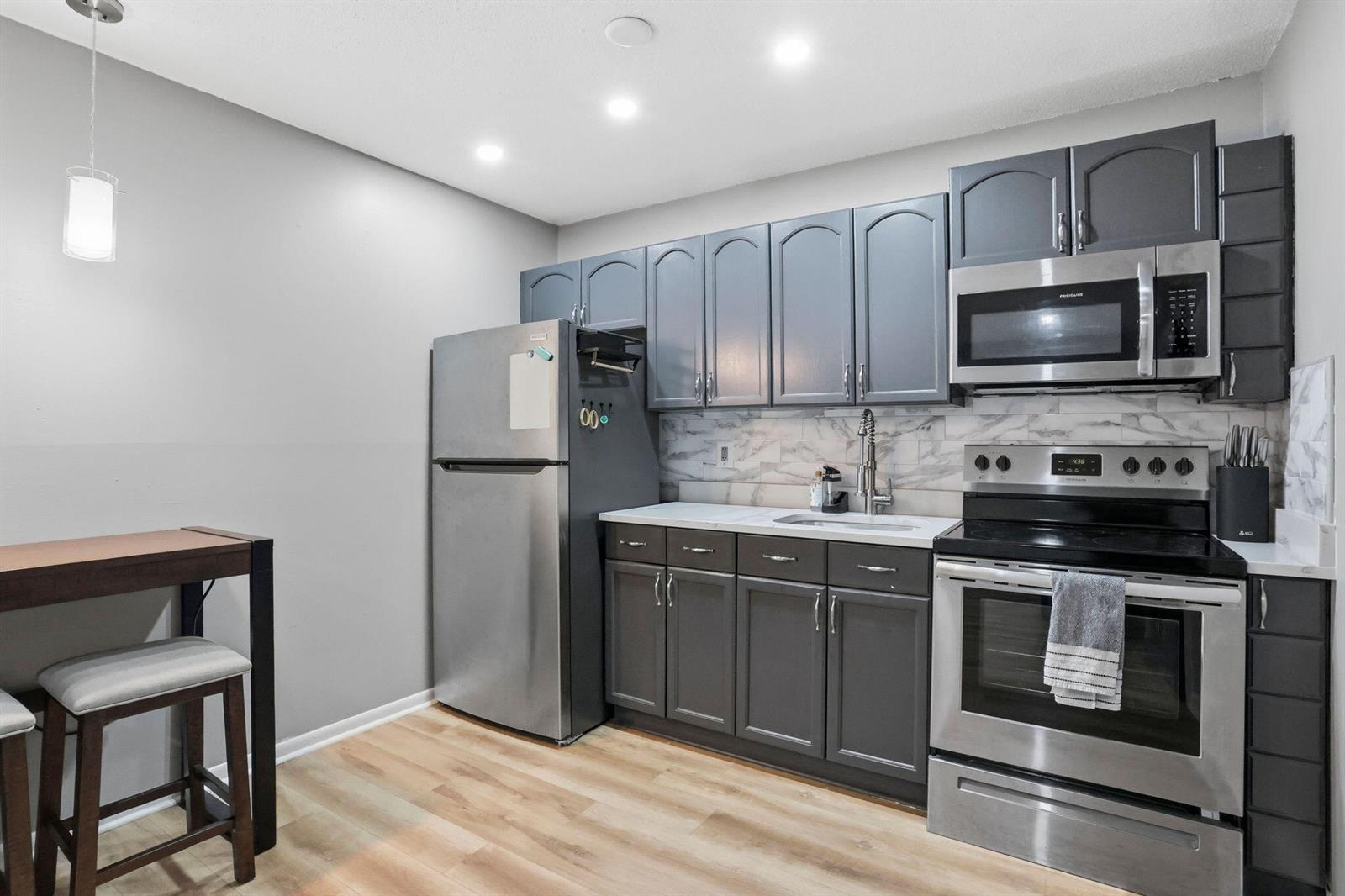 A kitchen features gray cabinets, stainless steel appliances, a marble-look backsplash, and light wood flooring — 1204 S Lake Drive E # 3, Lantana FL 33462, LANTANA, FL