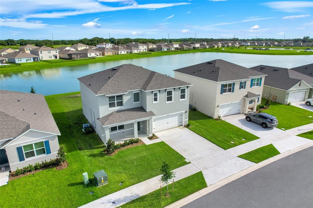 An aerial view shows two-story suburban houses with driveways and lawns bordering a large pond — 5252 MASSER ROAD, ST CLOUD, FL