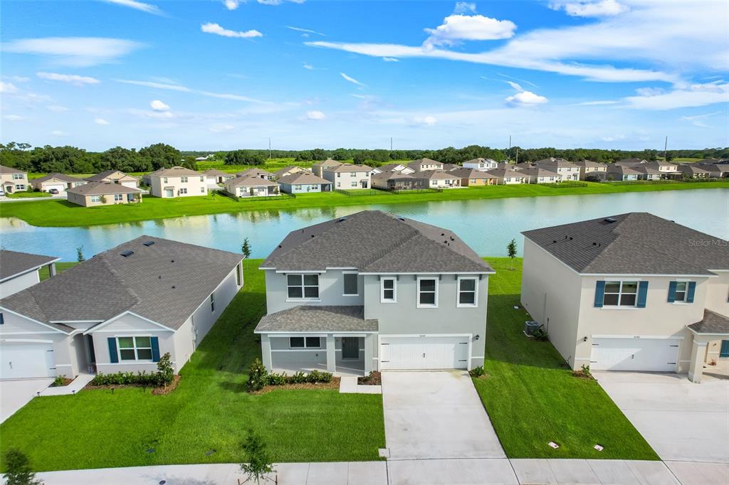 An aerial view shows a two-story suburban house with a gray exterior and lakefront backyard — 5252 MASSER ROAD, ST CLOUD, FL