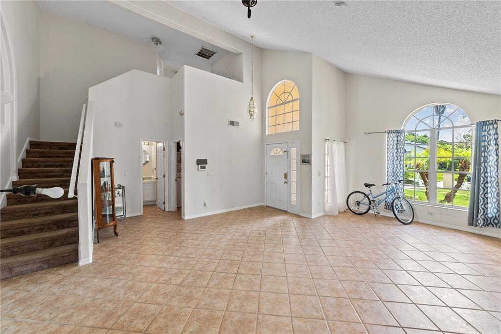 A high-ceilinged foyer features tile flooring, a staircase, a front door, and large windows — 3840 BECONTREE PLACE, OVIEDO, FL