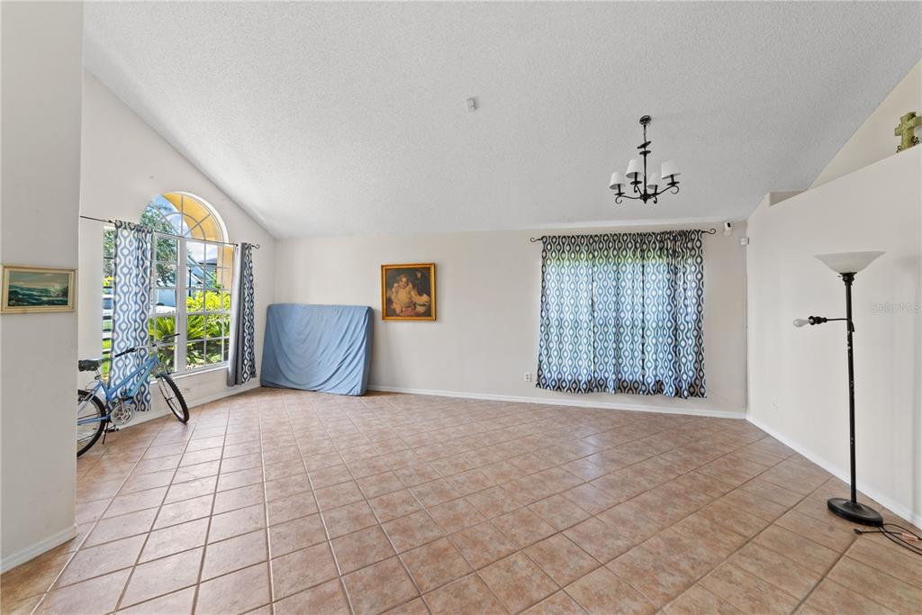A spacious living room features vaulted ceilings, tile flooring, a large arched window, and curtains — 3840 BECONTREE PLACE, OVIEDO, FL