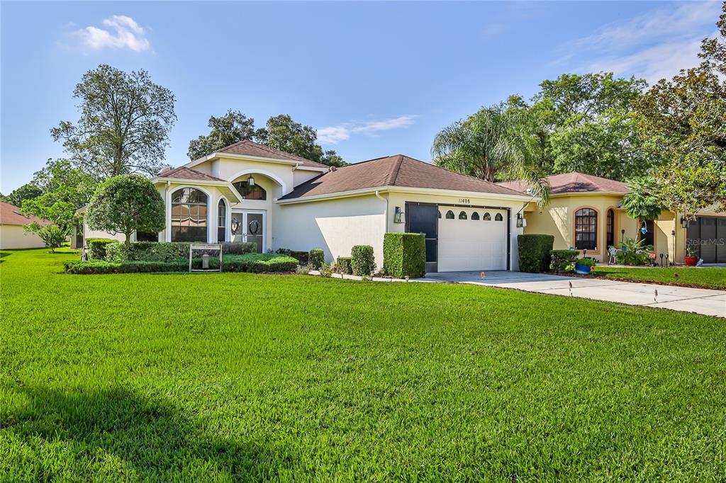 A single-story house with a white stucco exterior, a two-car garage, and a green lawn — 11408 DEERCROFT COURT, SPRING HILL, FL