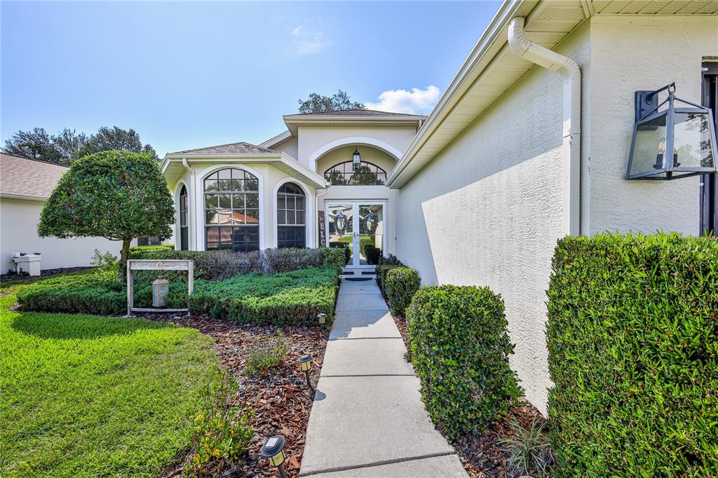 A concrete walkway leads to the front entrance of a house with a stucco exterior — 11408 DEERCROFT COURT, SPRING HILL, FL