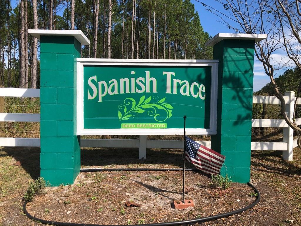 A green sign for Spanish Trace stands between two green pillars with a small flag — 1.77 acres NW 73 STREET, CHIEFLAND, FL