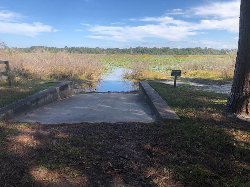 A concrete boat ramp leads into a marshy lake surrounded by trees and tall grass — 1.77 acres NW 73 STREET, CHIEFLAND, FL