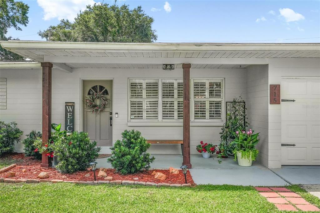 The exterior of a single-story house features a covered porch, wooden posts, and landscaped beds — 715 STEELE AVENUE, SOUTH DAYTONA, FL