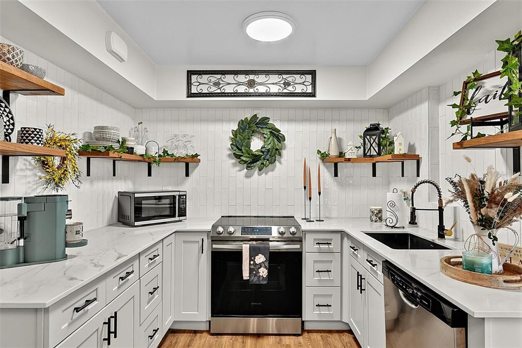 A kitchen features white cabinets, marble-look countertops, a subway tile backsplash, and stainless steel appliances — 715 STEELE AVENUE, SOUTH DAYTONA, FL