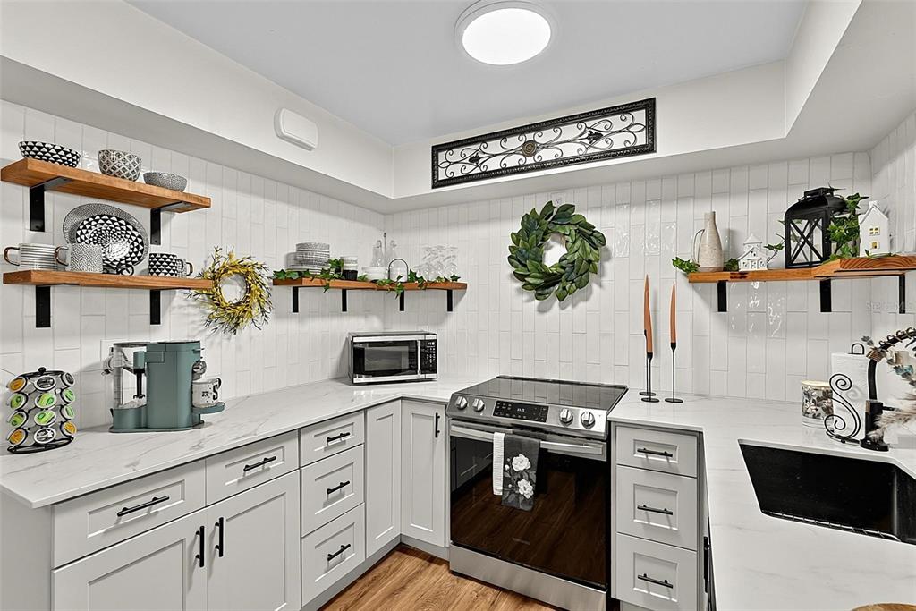 A kitchen features white cabinets, marble countertops, open wood shelving, and a stainless steel stove — 715 STEELE AVENUE, SOUTH DAYTONA, FL