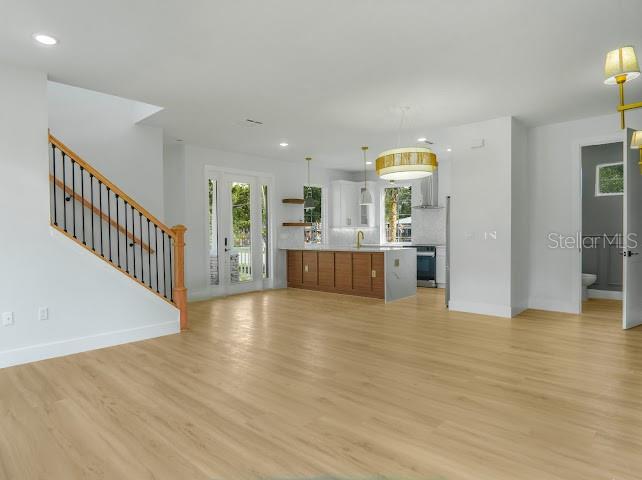 An open-concept living area features light wood flooring, a staircase with black railings, and a kitchen — 38 S POLLARD STREET, OAKLAND, FL