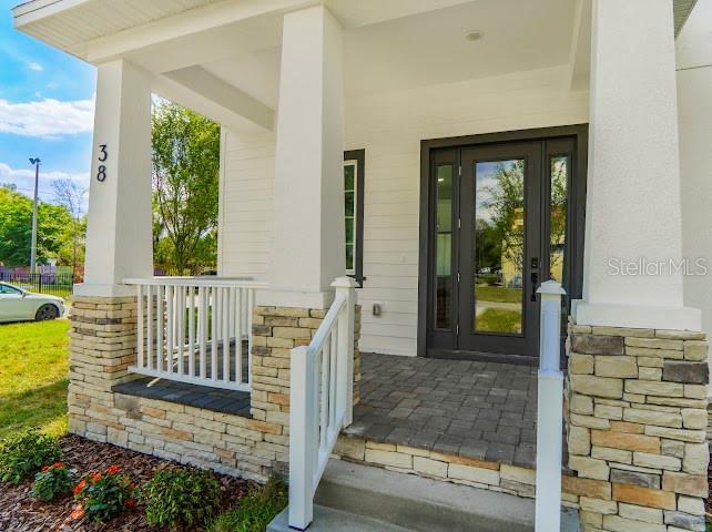 The front porch of a house features stone pillars, a white railing, and a glass-paneled door — 38 S POLLARD STREET, OAKLAND, FL