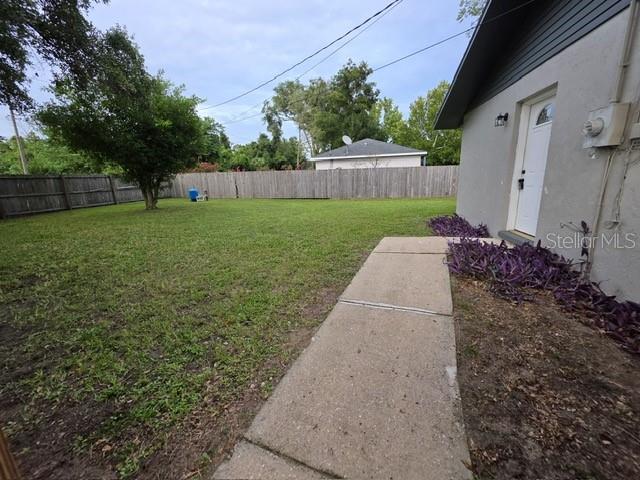 A concrete walkway leads to a white exterior door alongside a grassy backyard with fencing — 6881 NW 14TH AVENUE, OCALA, FL