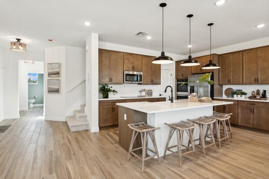 A kitchen features wood cabinets, a white island with four stools, and light wood flooring — 194 SE Birch Terrace # 0316, Stuart FL 34997, STUART, FL