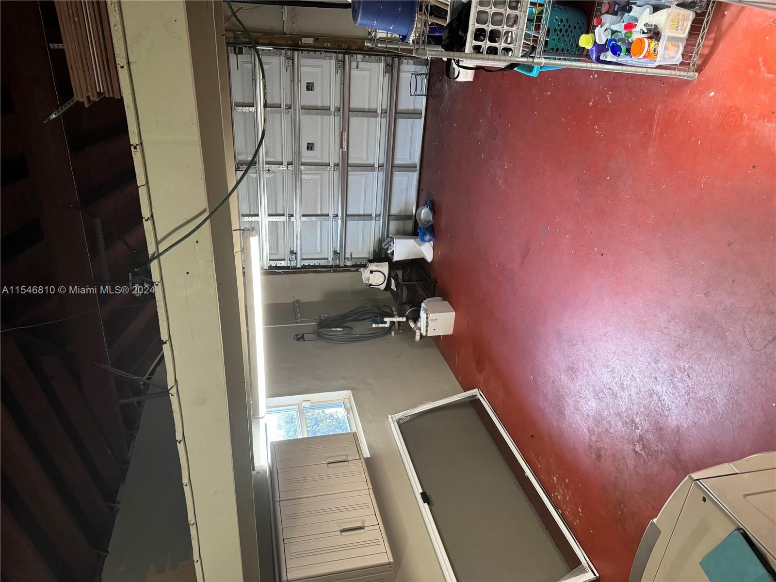 A garage with a red painted floor, a white sectional door, and storage shelving — 206 Ponce De Leon Blvd, Coral Gables FL 33134, CORAL GABLES, FL