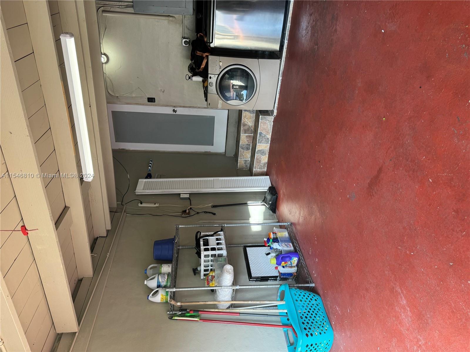 A garage space features a red concrete floor, a laundry unit, and metal storage shelving — 206 Ponce De Leon Blvd, Coral Gables FL 33134, CORAL GABLES, FL