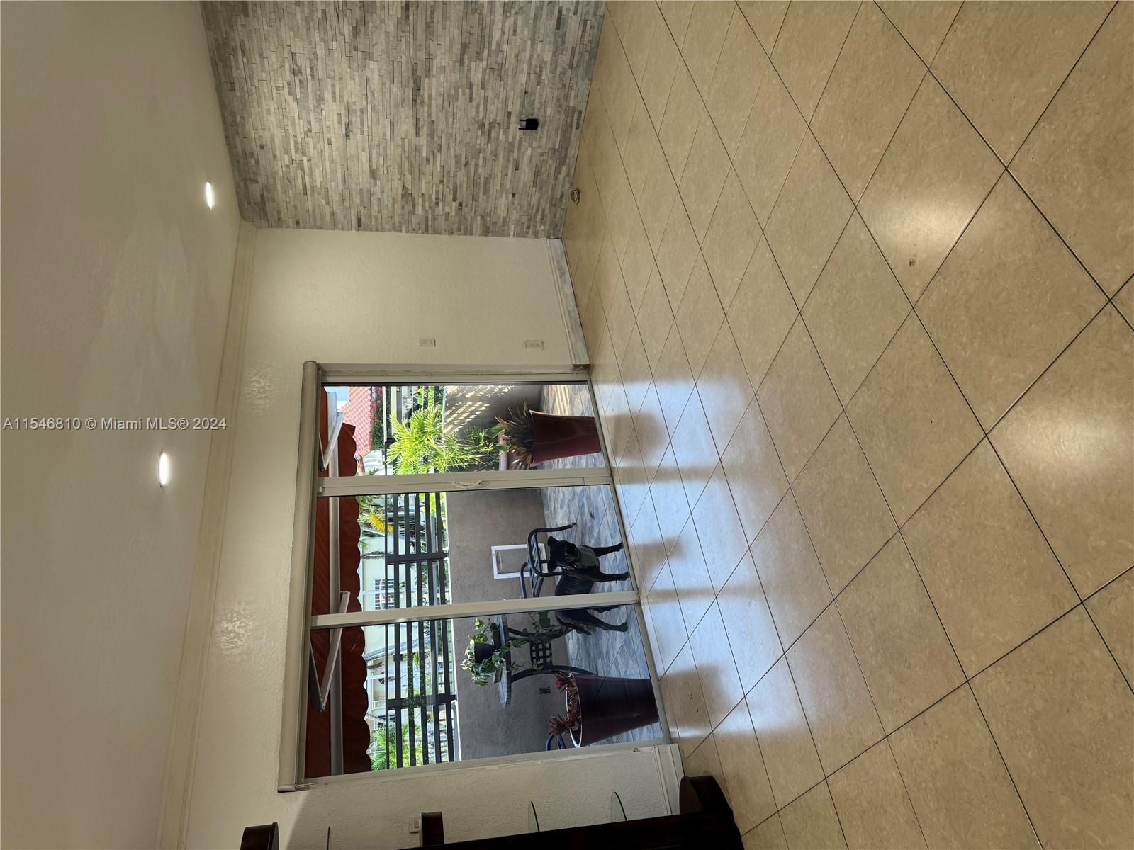 A room with beige tile flooring and a textured stone accent wall faces a patio — 206 Ponce De Leon Blvd, Coral Gables FL 33134, CORAL GABLES, FL