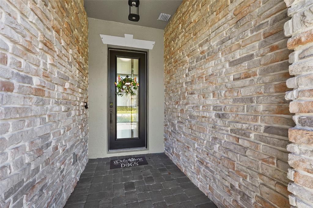 A stone-walled entryway features a dark front door with a glass panel and a doormat — 7208 GREAT EGRET BOULEVARD, SARASOTA, FL