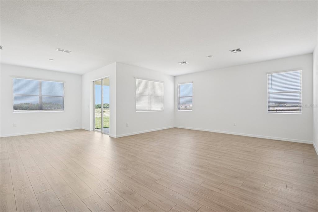 An empty living room with light wood-look flooring, white walls, and several windows — 4664 BARBERRY AVENUE, LAKELAND, FL