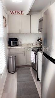 A galley kitchen features light gray cabinets, stainless steel appliances, and light wood-look flooring — 4733 CLUB CIRCLE, LAKESHORE, FL