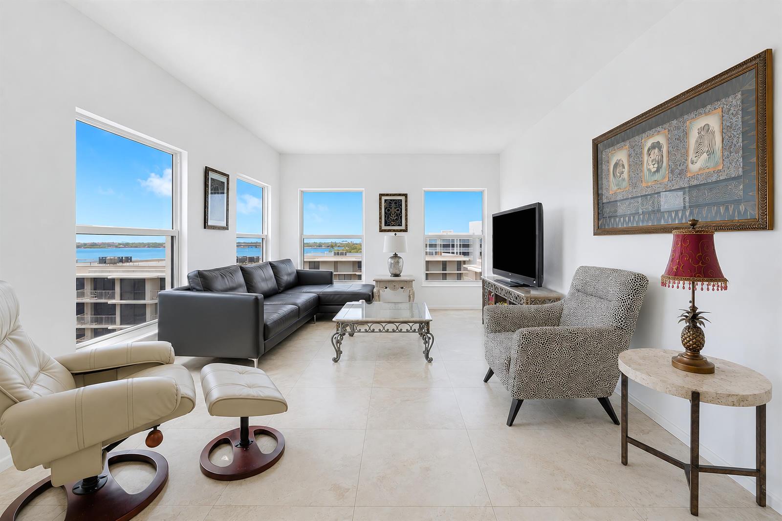 A living room with a black sectional, patterned armchair, television, and windows overlooking the water — 3230 S Ocean Boulevard # 607, Palm Beach FL 33480, PALM BEACH, FL