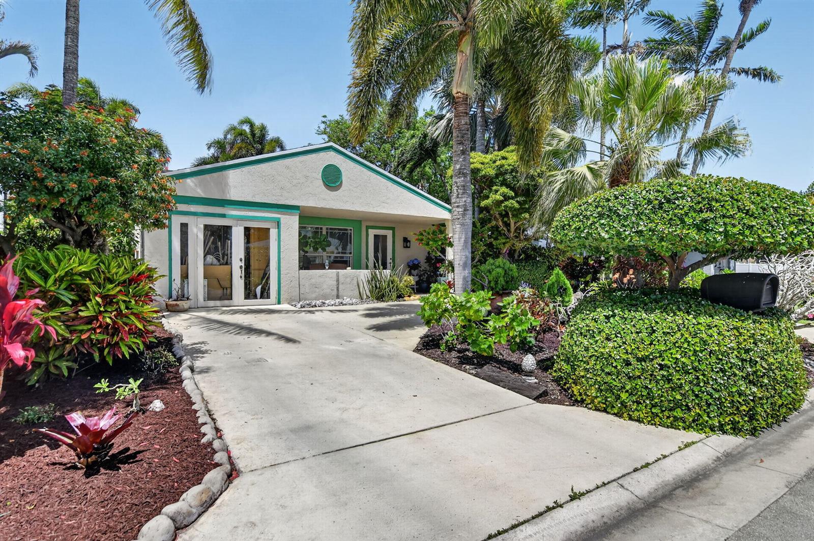 A single-story house with a concrete driveway, green trim, and lush tropical landscaping — 8353 Huntsman Place, Boca Raton FL 33433, BOCA RATON, FL