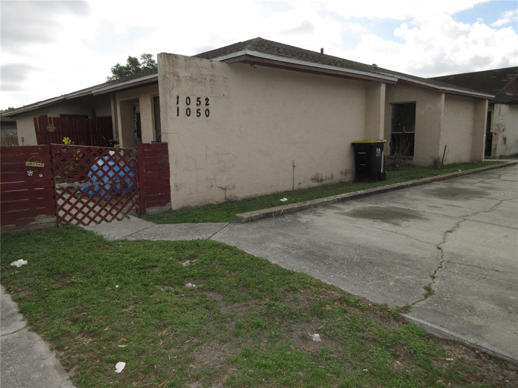 A single-story duplex with a concrete driveway, a red lattice fence, and tan stucco walls — 1050 CAPTIVA POINT, LAKELAND, FL