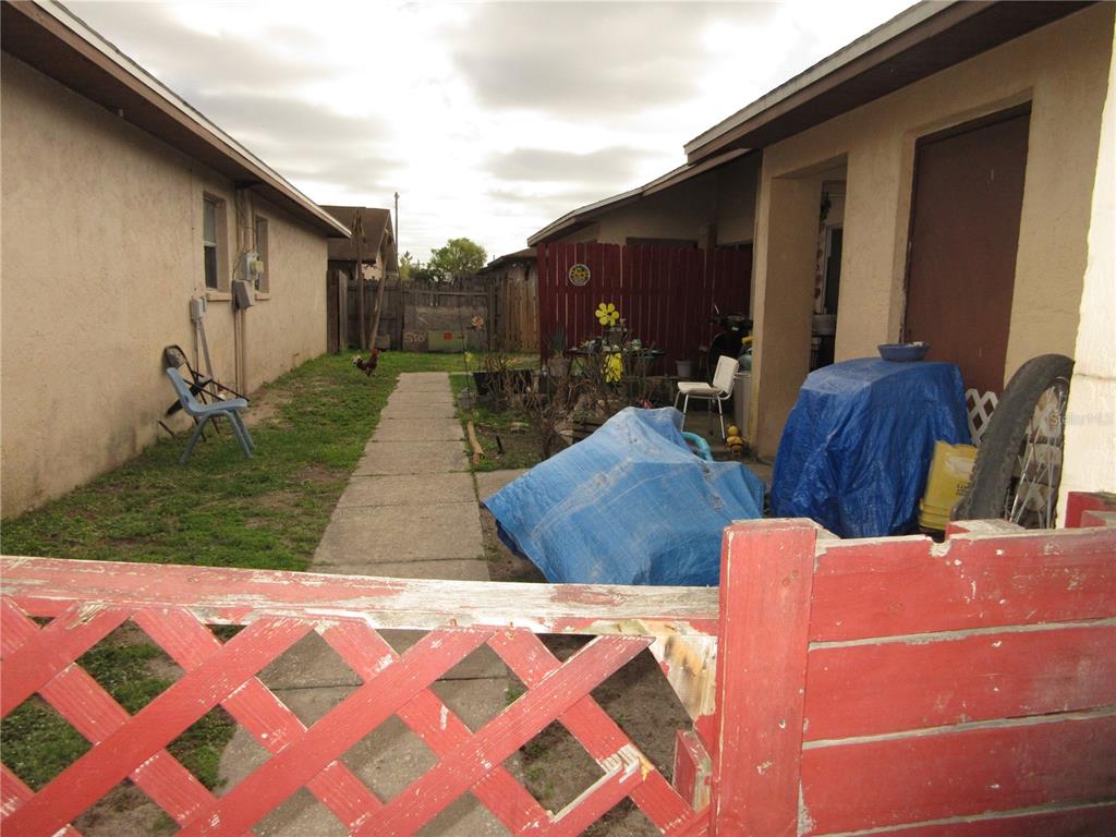 A narrow backyard path leads between two stucco buildings toward a red wooden fence — 1050 CAPTIVA POINT, LAKELAND, FL