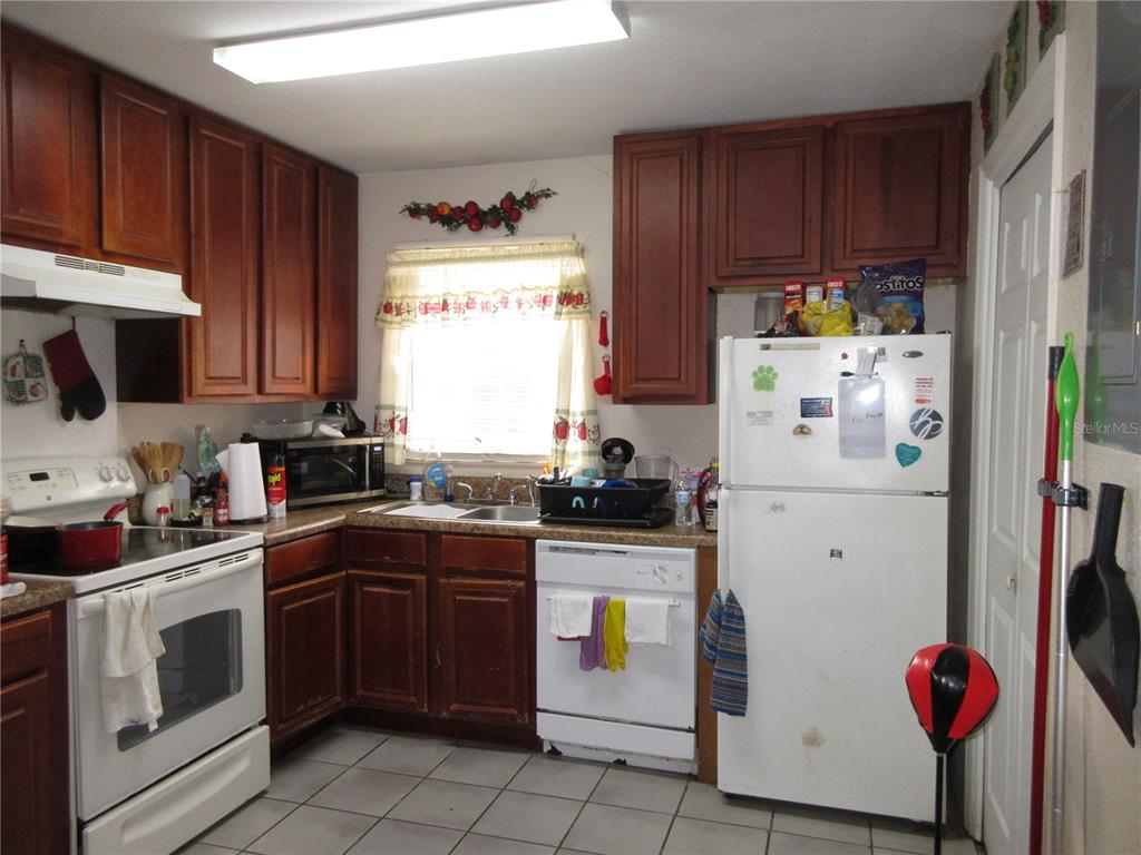 A kitchen features dark wood cabinets, white appliances, tile flooring, and a window above the sink — 1050 CAPTIVA POINT, LAKELAND, FL