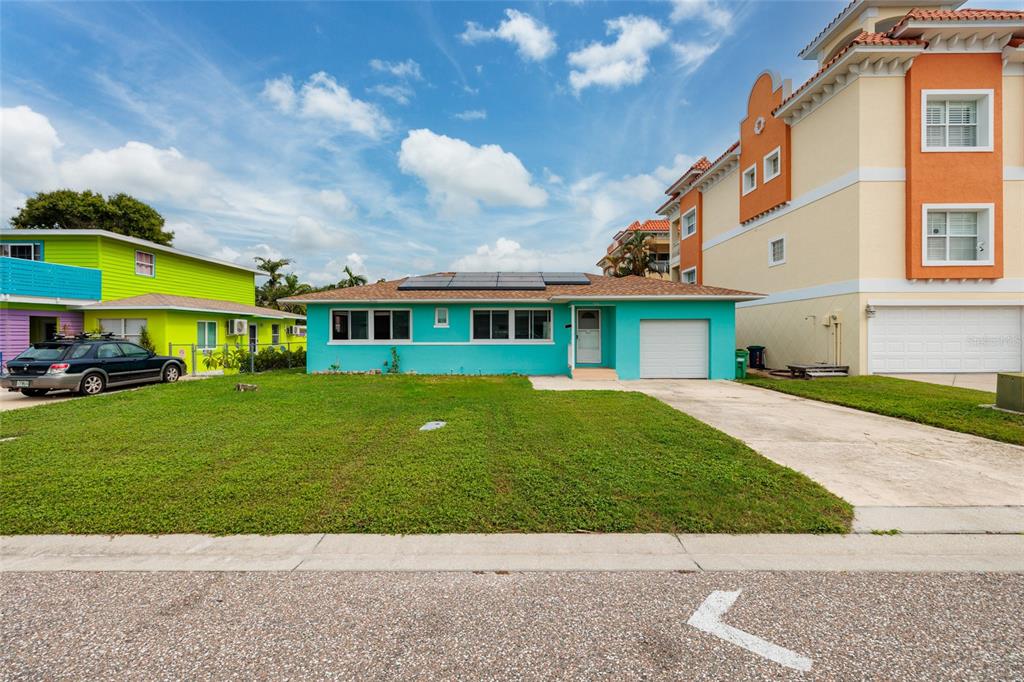 A turquoise single-story house with solar panels sits between a lime green house and a townhouse — 136 175TH TERRACE DRIVE E, REDINGTON SHORES, FL