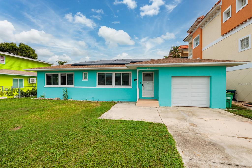 A single-story turquoise house with a white garage door and solar panels on the roof — 136 175TH TERRACE DRIVE E, REDINGTON SHORES, FL