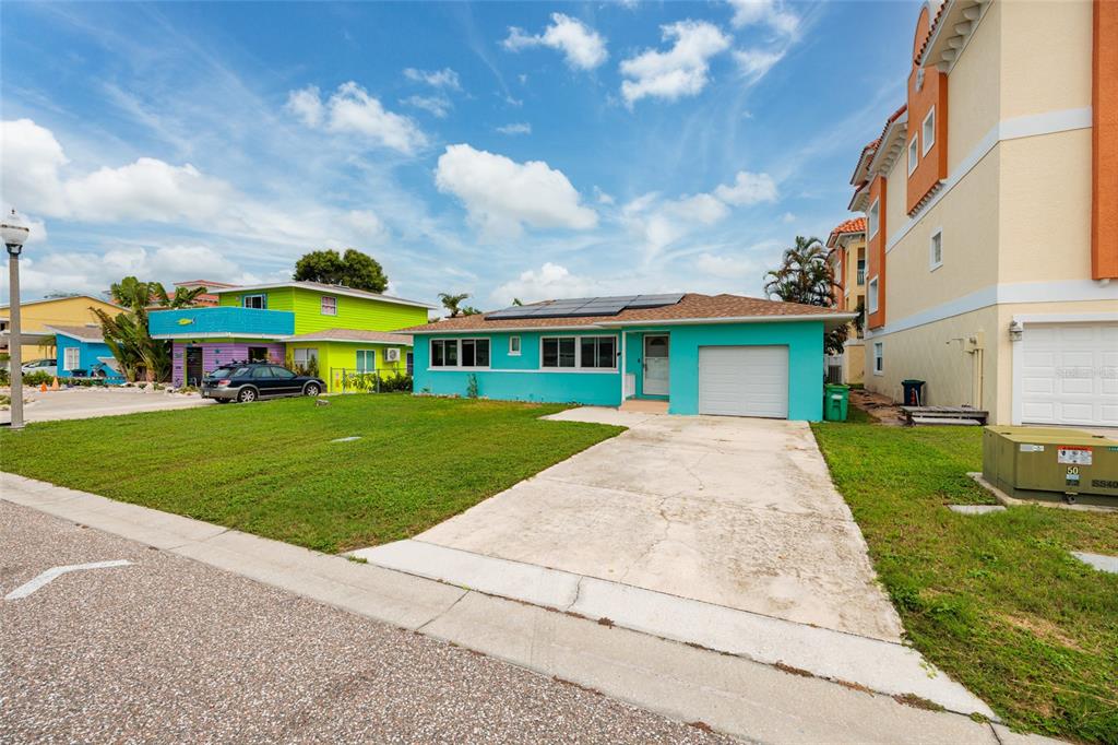 A teal single-story house with a concrete driveway, solar panels, and a white garage door — 136 175TH TERRACE DRIVE E, REDINGTON SHORES, FL