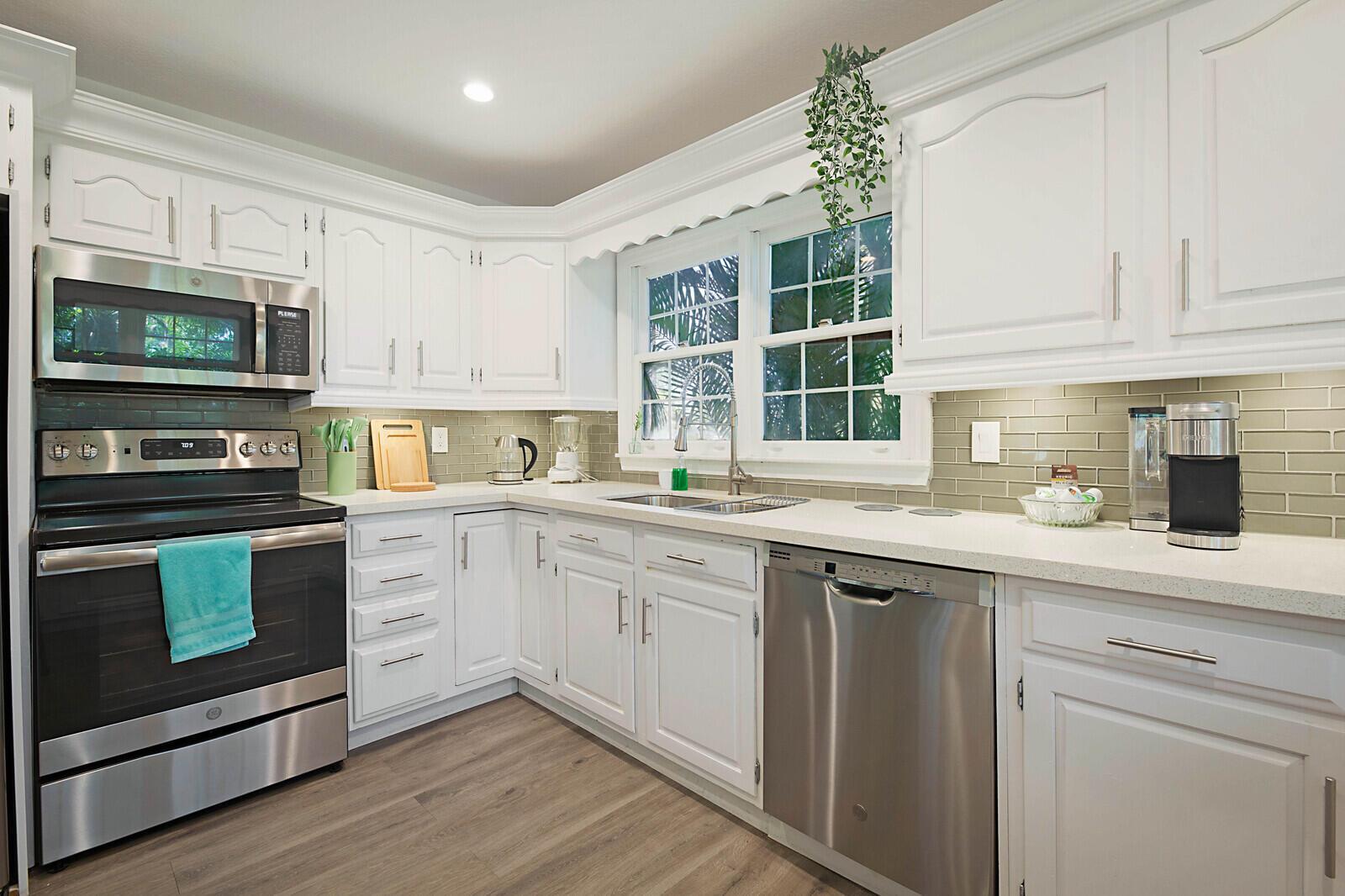 A kitchen features white cabinets, stainless steel appliances, a subway tile backsplash, and wood flooring — 13346/13026 Casey Road, FL 33470, FL