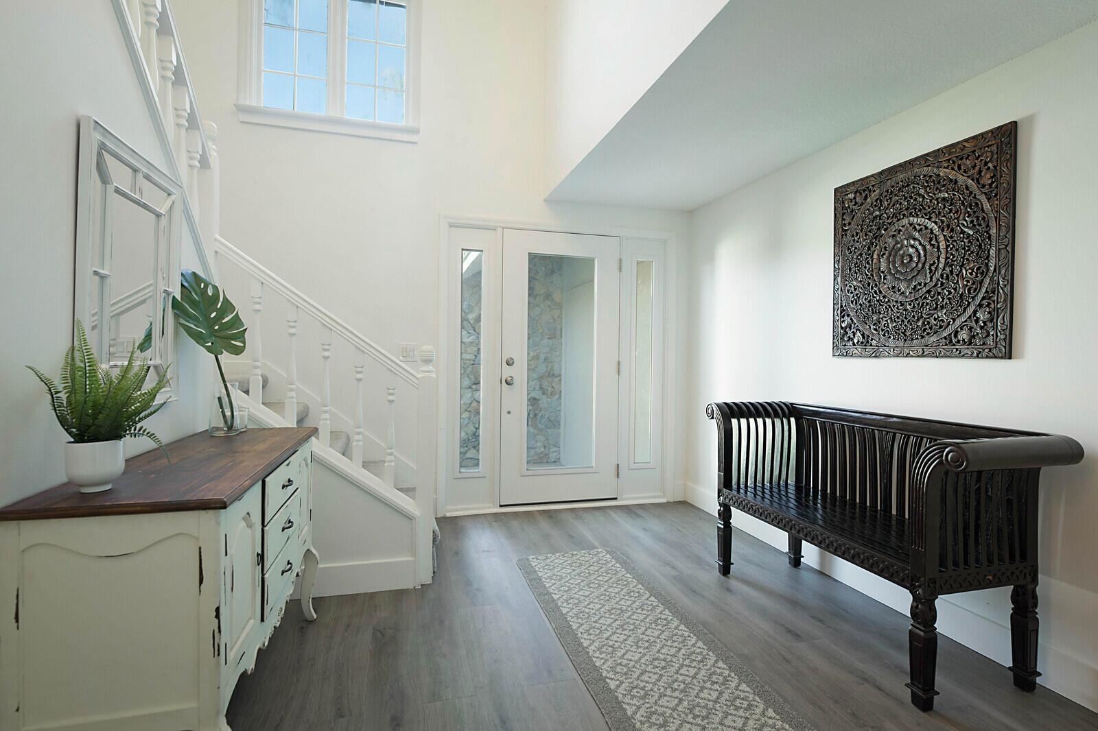 A bright entryway features a staircase, a wooden bench, a decorative wall panel, and flooring — 13346/13026 Casey Road, FL 33470, FL