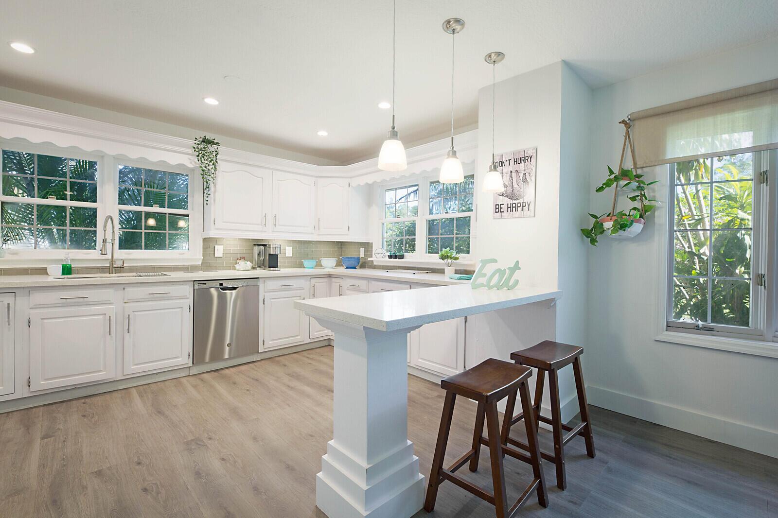 A bright kitchen features white cabinets, a breakfast bar with two stools, and large windows — 13346/13026 Casey Road, FL 33470, FL