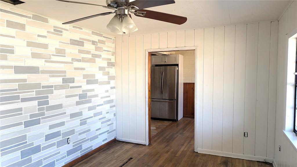 A room with a stone-patterned accent wall, wood flooring, and a doorway leading to a kitchen — 3425 IRENE STREET, MELBOURNE, FL