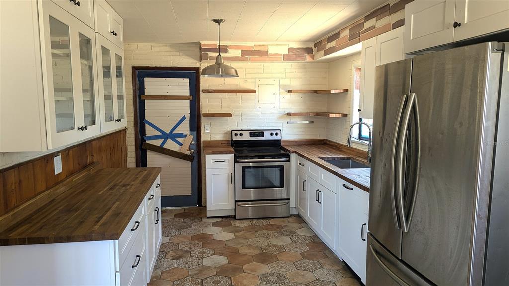 A kitchen features white cabinets, butcher block countertops, stainless steel appliances, and hexagonal floor tiles — 3425 IRENE STREET, MELBOURNE, FL