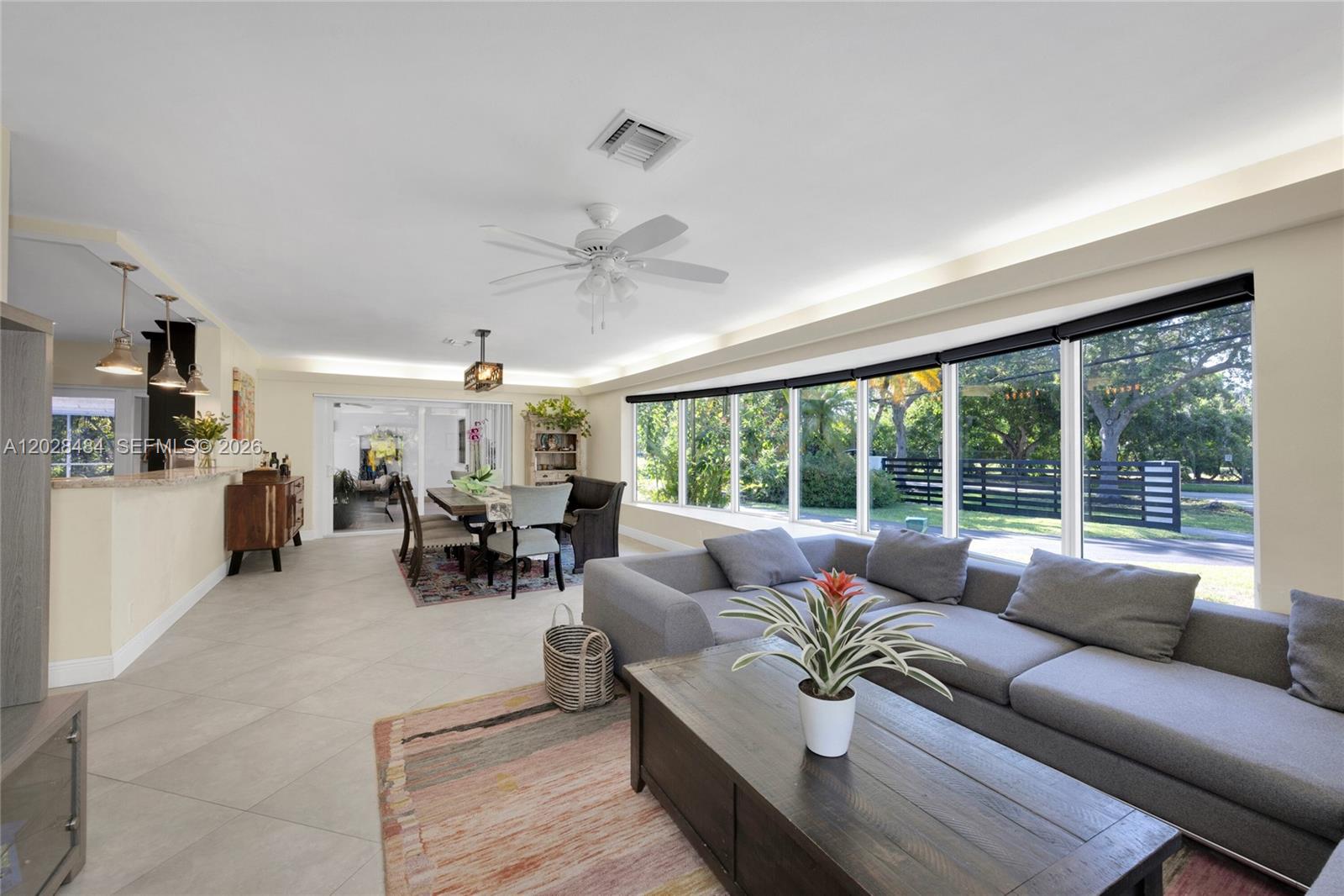 A living and dining area features tile floors, a gray sectional, and large picture windows — 6970 SW 124th St, Pinecrest FL 33156, PINECREST, FL