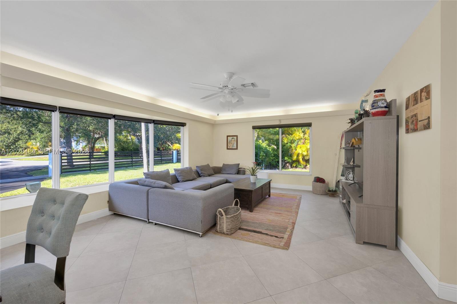 A living room features a large gray sectional sofa, a coffee table, and expansive windows — 6970 SW 124th St, Pinecrest FL 33156, PINECREST, FL